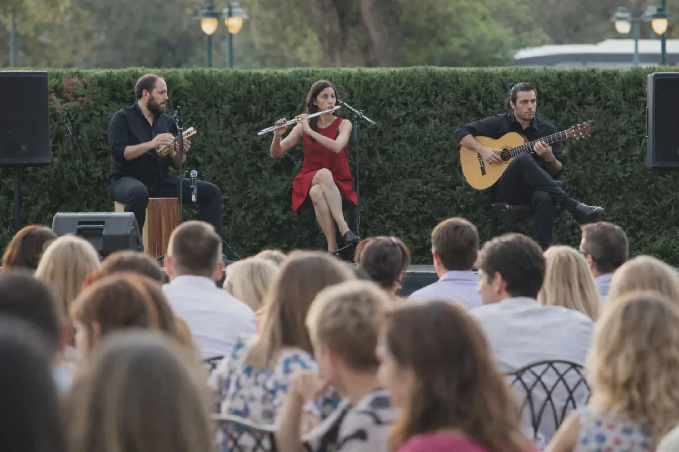 Live flamenco trio with guitar, flute and cajón performing outdoors for a seated corporate audience at an evening reception