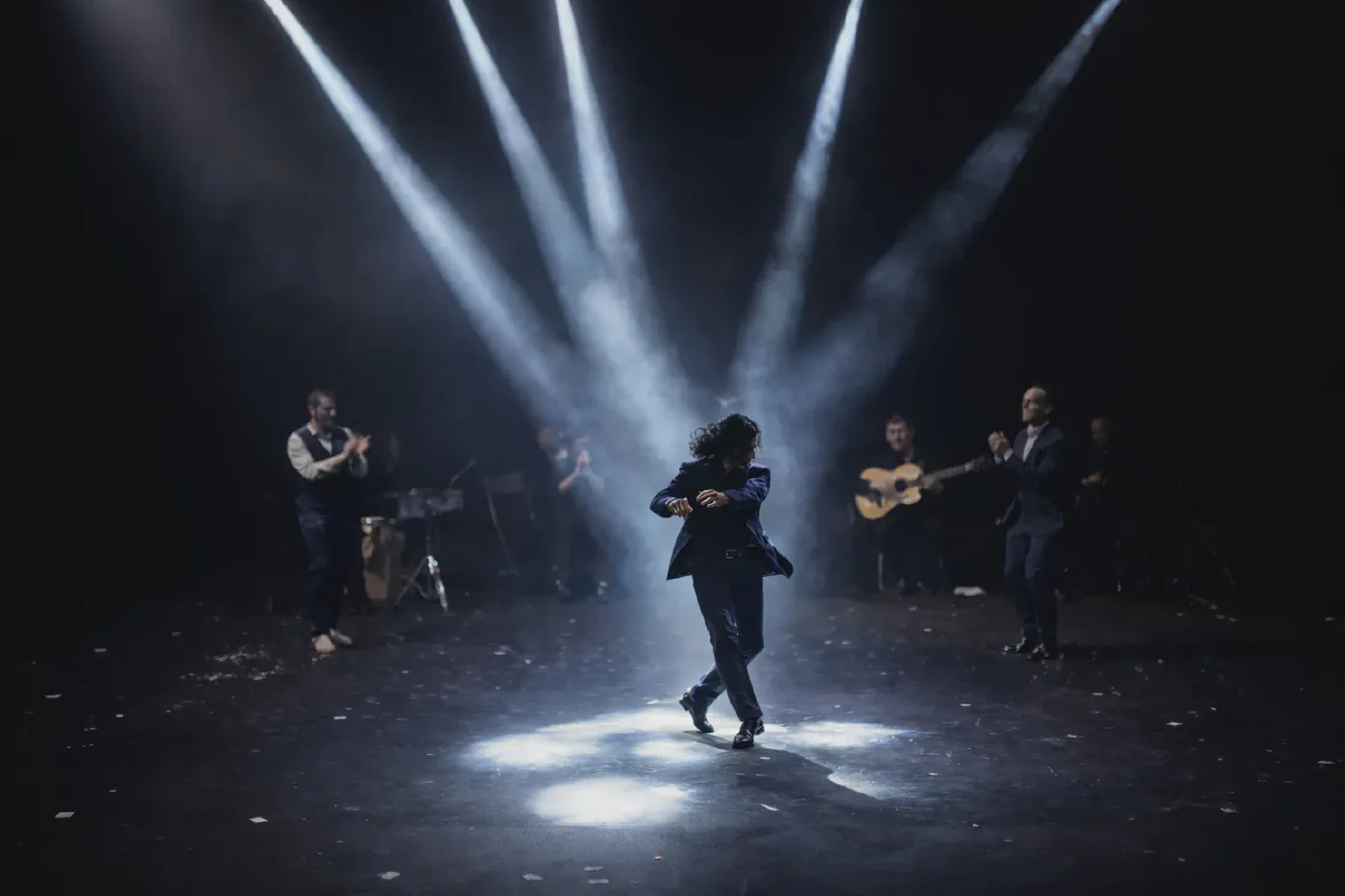 Bailador flamenco bajo focos en escenario con músicos